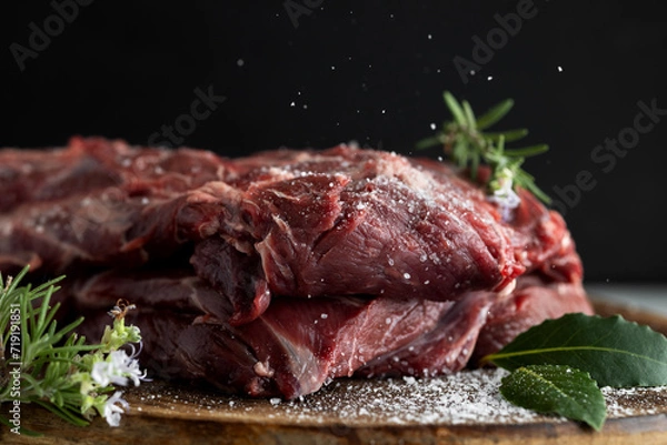Fototapeta Food Composition Neck part of reindeer meat on a wooden chopping board in close-up. Salt is pouring out