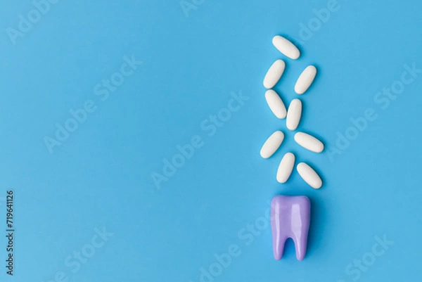 Fototapeta Dental care concept. Toothache pills. Purple tooth model and medical tablets on a blue background with copy space. Close up view of white pills and tooth model on blue background.