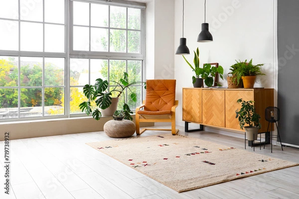 Fototapeta Interior of living room with green plants, commode and armchair