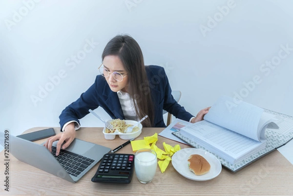 Fototapeta Asian business woman busy with work, where she eats while working because she hastened to complete the work according to the goal, to business and work so busy that you don't have time to eat concept.