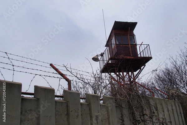 Obraz A concrete fence with a metal fence and an observation tower for armed guards to a prison or military plant