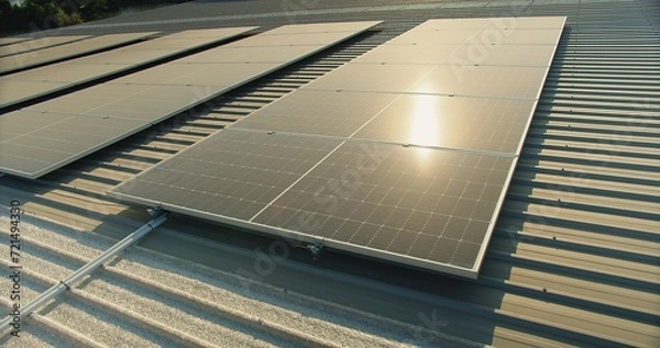 Obraz solar panels on a corrugated metal roof reflecting sunlight, showcasing alternative energy, Close-up of solar panels on an industrial building's roof capturing sunlight for energy.