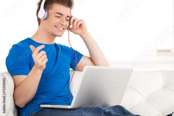 Fototapeta Happy man in headphones with laptop relaxing on sofa at home.