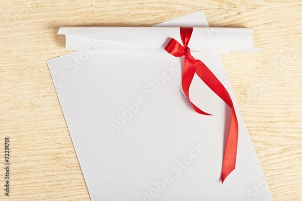 Fototapeta Scroll of paper with a red ribbon on a wooden surface.