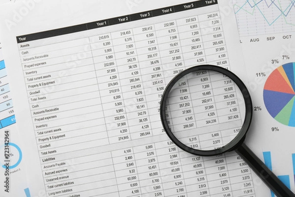 Fototapeta Magnifying glass on accounting documents, top view