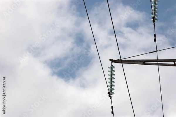 Fototapeta High voltage grid electric power line electricity pilon traverse glass insulators and transmission wires, large detailed steel cables horizontal closeup, bright summer sky cloudscape background