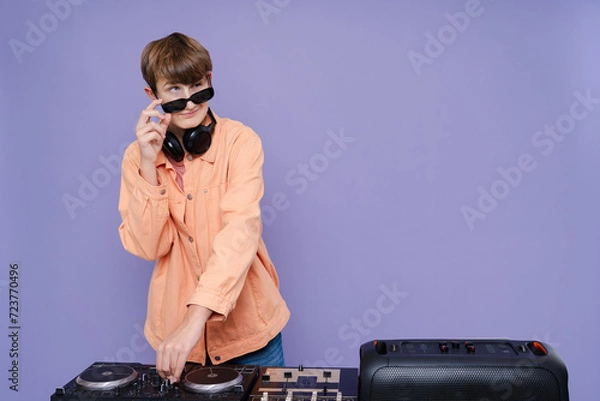 Fototapeta Cool charming boy with headphone and sunglasses play music on a turntable isolated over bright color background