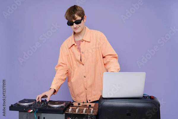 Fototapeta Cheerful teenager posing and listening music  in stylish clothes and glasses on a color background.
