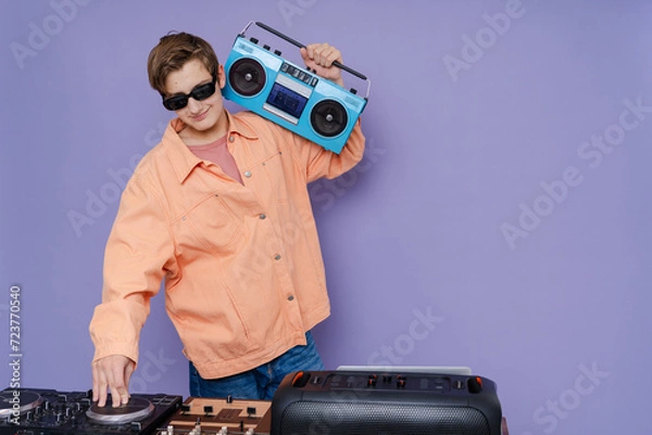 Fototapeta Photo of young DJ hold boom box  and playing music on a turntable  on color background