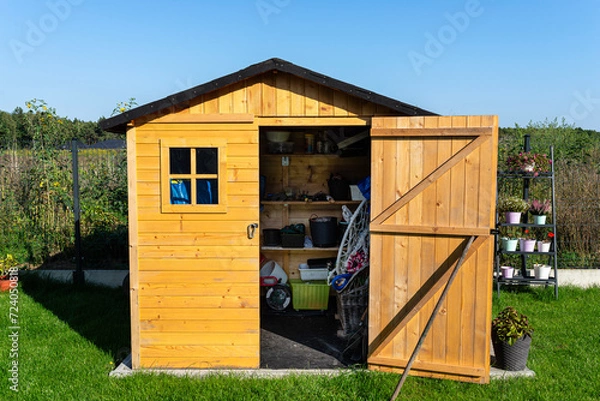 Obraz A wooden garden shed standing on a concrete foundation in a garden, flowers and tools visible.