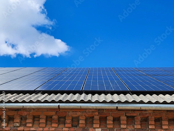 Obraz Blue solar panels on an eco-friendly house roof, harnessing the suns energy to generate clean power, creating a positive impact on the environment against a serene blue sky with scattered clouds.