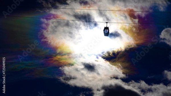 Fototapeta Cloud iridescence, or rainbow clouds, with a cable car in front.