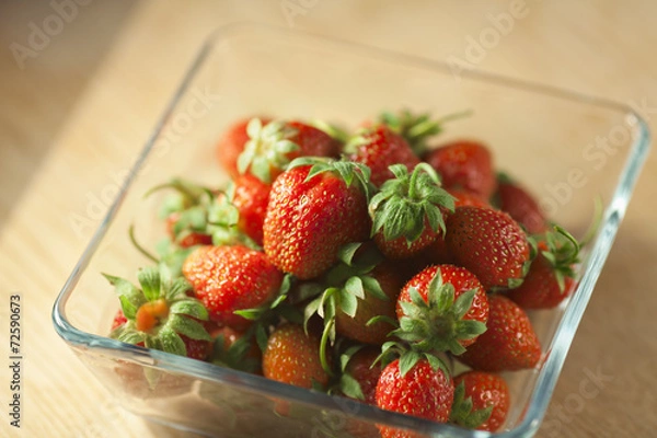 Fototapeta Strawberry fruit in a glass container on a wooden surface. Bokeh