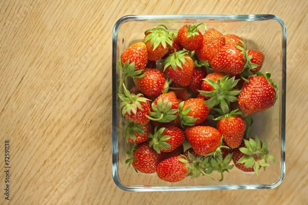 Fototapeta Strawberry fruit in a glass container on a wooden surface. Bokeh