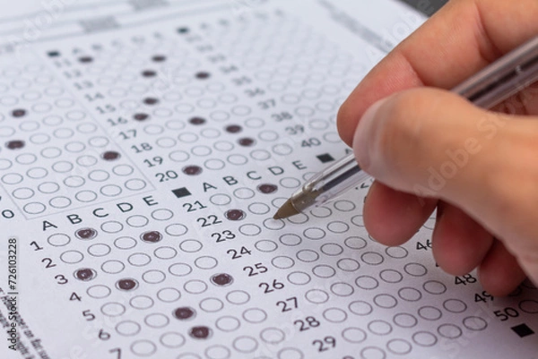 Obraz Hand filling out an exam answer sheet with a pen, concept for public and entrance exams.