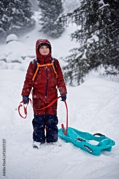Fototapeta Portrait of a young European boy 7 - 9 years old in the warm winter jacket standing on the snowy winter background with sledge