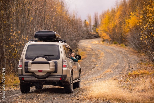 Fototapeta A woman sitinng in a SUV on а scenic autumn road in the forest and smiling