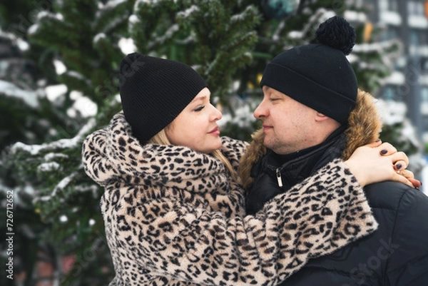 Fototapeta Love romantic couple lovestory. Man hugging woman, kissing girl in Christmas winter fur trees decoration. Romantic date. Walking,having fun. Stylish clothes,fur leopard print coat, black jacket, hat