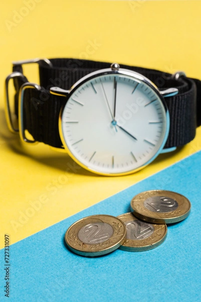 Fototapeta A hand watch with a white shield and tips lying on a yellow-blue background. Next to the Polish coins of PLN. Photo concept