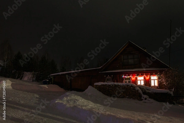 Fototapeta View from a hill on wooden houses covered snow at night. Scenery of ski resort with lights. Theme of travel.
