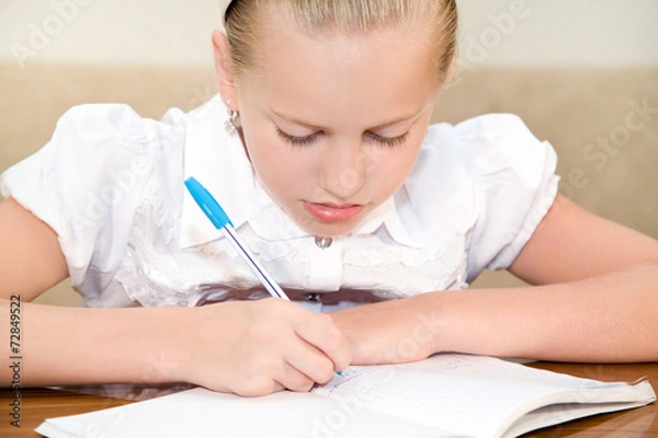 Fototapeta Schoolgirl child writes in a notebook