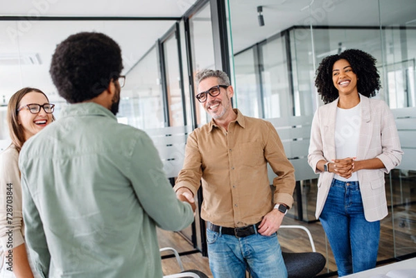 Fototapeta A friendly office environment is depicted where a team greets each other, shaking hands, showcasing the warmth and positive relationships between colleagues in a modern business setting.