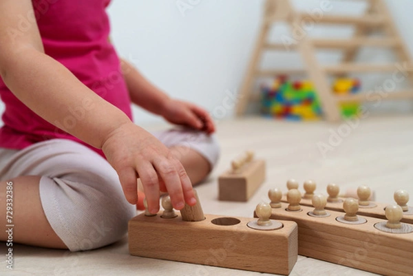 Fototapeta A 2.5 year old child sorts shapes of different sizes. Wood childrens game by Montessori system. Wooden knobbed cylinders for preschool and kidergarten playing.
