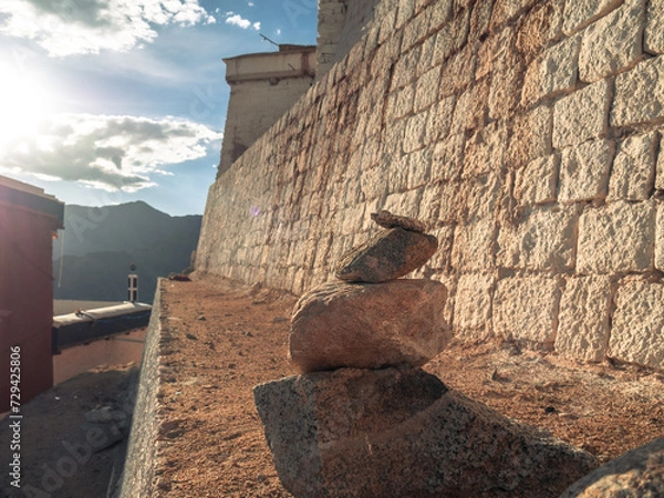 Obraz Rock cairns or Stacking stones in evening sunlight, with wall of Tsemo fort at background.