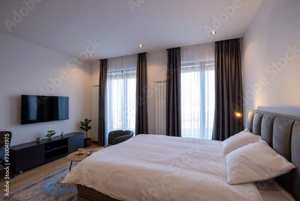 Fototapeta Interior of a bedroom with large master bed and wall mouted tv