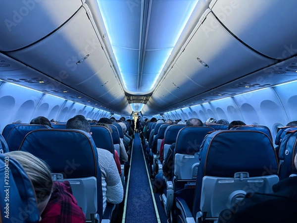 Obraz An airplane cabin with beautiful lighting and passengers sitting with their backs towards the camera