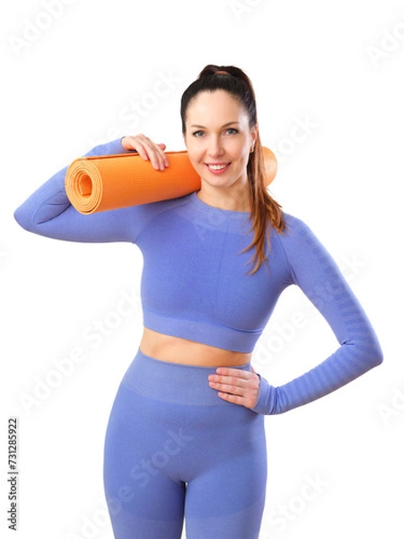 Fototapeta A fit woman with a ponytail, dressed in a coordinated blue activewear set, confidently holding an orange yoga mat, ready for a fitness session. Isolated on white.