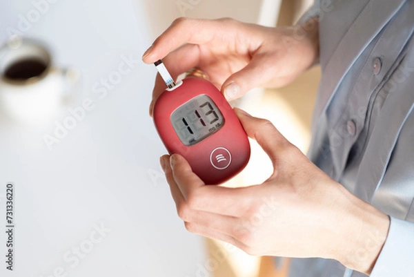 Obraz A young woman measures her blood sugar level using a glucometer.