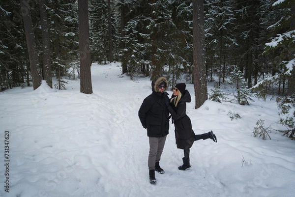 Fototapeta A young couple in sunglasses walks in the forest on a winter day.