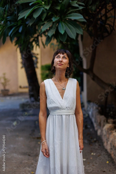 Fototapeta Tourist on vacation. Woman with an expression of freedom and pleasure. A girl in a white dress walks along the streets of the old city.