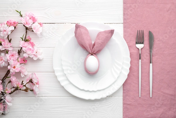 Fototapeta Easter lunch invitation. Festive table setting with pink spring flowers and cutlery. Bunny made of linen napkin and egg. Happy Easter holiday, menu concept. Empty plates, white wooden background.