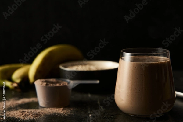 Obraz Chocolate Protein Power Cocktail with Ripe Bananas, Whole Oats, and Creamy Milk in a Modern Glass, Ideal for Post-Workout Recovery, Set Against a Dark, Textured Background