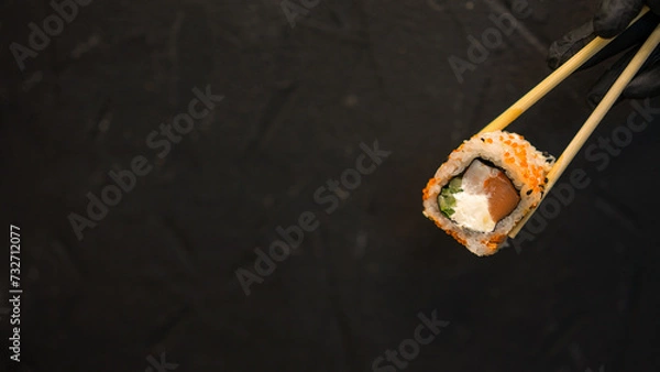 Fototapeta Sushi rolls on a dark background. The hand holds the roll. Sushi sticks