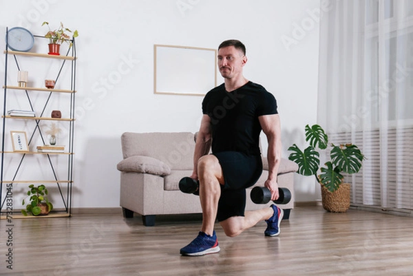 Obraz Bodybuilder training at home, doing lunges with dumbbells. Young man performing physical exercises in his living room. Close up, copy space, background.