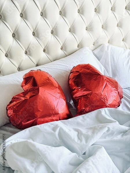 Obraz Two red heart-shaped balloons lie on a white bed in a retro bedroom. Wedding day or Valentine’s Day. Vertical image.	
