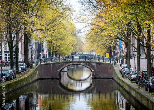 Fototapeta Peaceful morning of Amsterdam in the autumn with canal, bridge, buildings, bikes and trees.