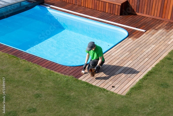 Fototapeta Exterior wooden pool deck painting, above view, person applying refreshing coat to poolside wood decking