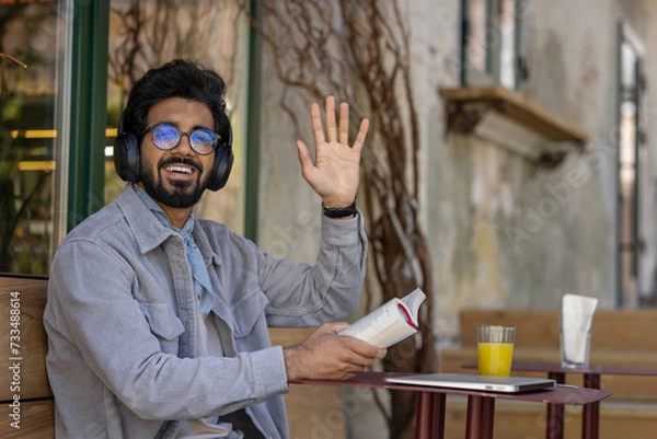 Obraz Dark-haired young hindu man in headphones with a book in hands