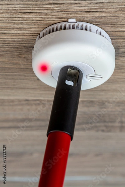 Fototapeta Checks smoke detector with a cleaning broom