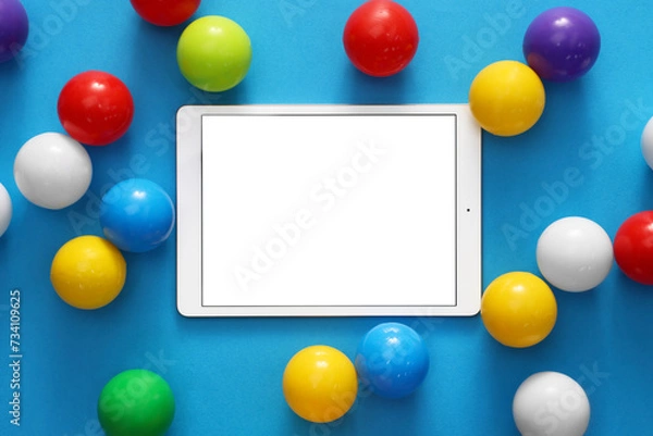 Fototapeta Modern tablet and balls on light blue background, flat lay. Space for text