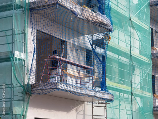 Fototapeta Persona trabajando en la construcción de un edificio pintando una pared, con redes de protección alrededor, primavera de 2024 Barcelona