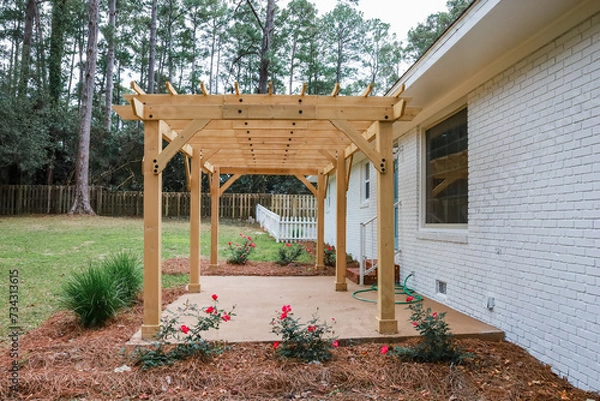 Fototapeta The rear back exterior of a newly painted and renovated white brick ranch style house with a large yard and a newly built wood arbor pergola for shade