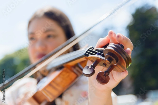 Fototapeta closeup of blurred unrecognizable woman tuning violin, focus on hand on pegs