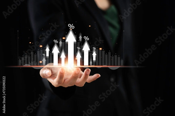 Fototapeta Businessman holds arrow and percentage icon with graph indicators for investment growth. Interest rates and dividends business financial investment Business growth, revenue, marketing and profits