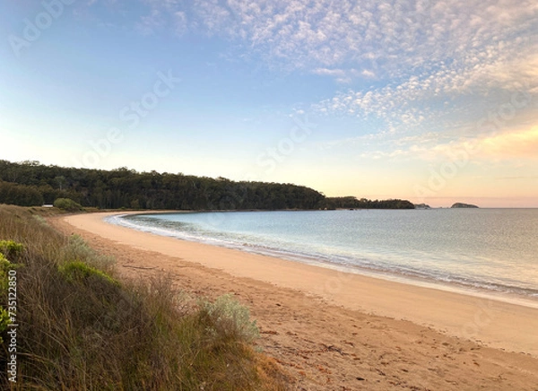 Fototapeta Sunrise on the beach. Dawn over the ocean. Morning rise at the beach. Tall grass near the shore. Waves on the sand.