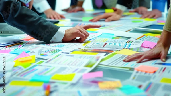 Fototapeta top view of a busy work table during a team meeting, with hands of diverse people working with colorful sticky notes